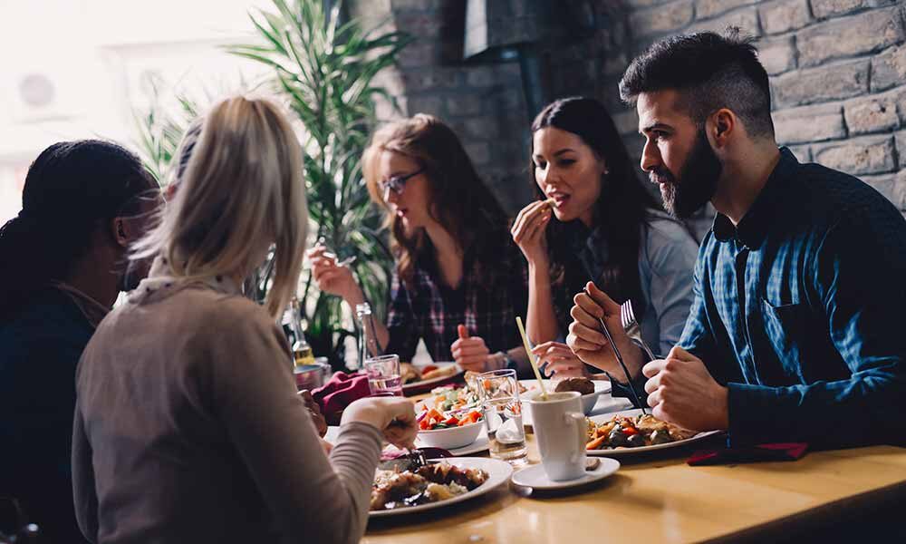 Fire personer nyter et måltid sammen ved et restaurantbord, med retter, drinker og samtaler i gang.