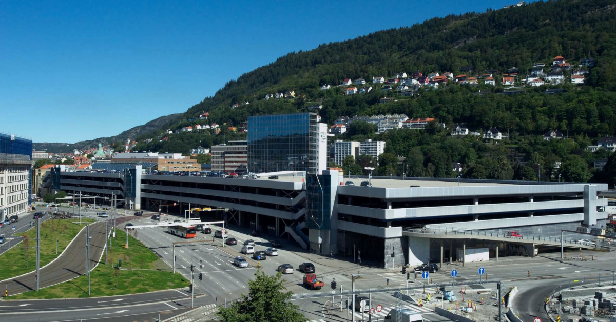feat-img-BG-40-ar Et stort parkeringshus med flere plan i et urbant område med omkringliggende veier, moderne bygninger og en skogkledd åsside i bakgrunnen.