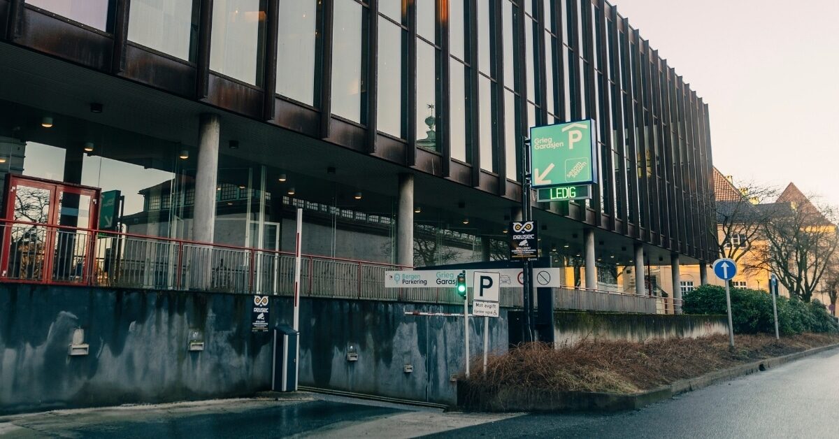 Moderne bygning med store vinduer, opphøyd fortau og flere parkeringsskilt. Viser innkjøringsfeltet til GriegGarasjen under Grieghallen.