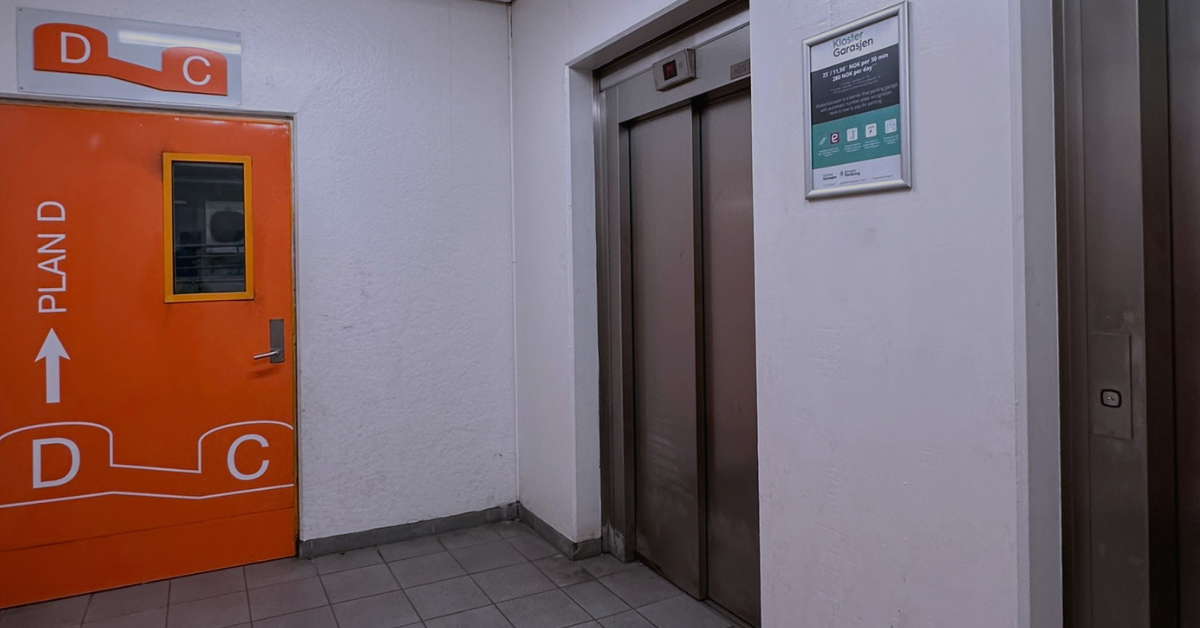 Gang med en knalloransje dør merket "Plan D" og en heis med skilt på veggen ved siden av.