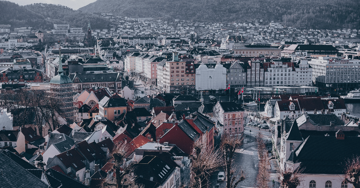 feat-img-hostferie Luftfoto av et europeisk bybilde med tettpakkede bygninger, røde og hvite hustak og omkringliggende åser. Overskyet himmel og nakne trær er synlige.