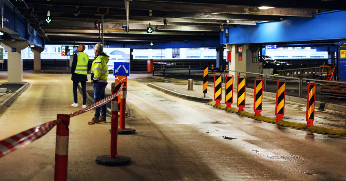 feat img template-1 (11) To arbeidere i vernevester står i et svakt opplyst parkeringshus og fører tilsyn med eiendomsdriftsaktiviteter. Trafikkkjegler og barrierer langs veien, reflekterer Bergen Parkerings forpliktelse til sikkerhet og effektivitet.