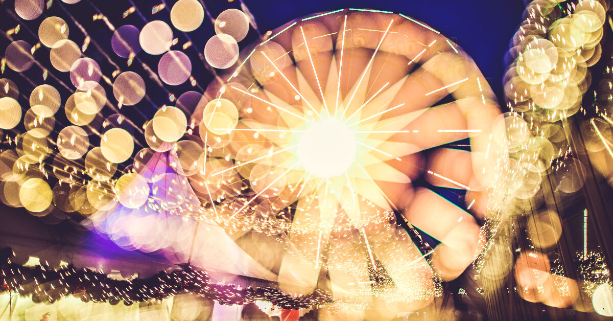Uskarpt bilde av et pariserhjul om natten med sterkt lys og en bokeh-effekt, som fanger en abstrakt, festlig scene som minner om julebyen-feiringen.