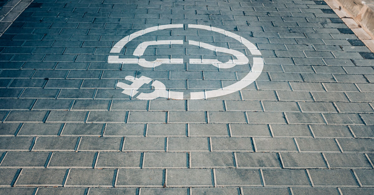 Ladesymbol for elbil malt på et brosteinsbelegg ved Bygarasjen.