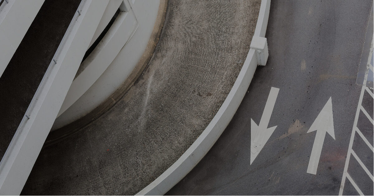 Luftfoto av en spiralbetongrampe nær Bergen sentrum, med to hvite retningspiler malt på den grå veibanen, som antyder effektive parkeringsmuligheter for bildeling.