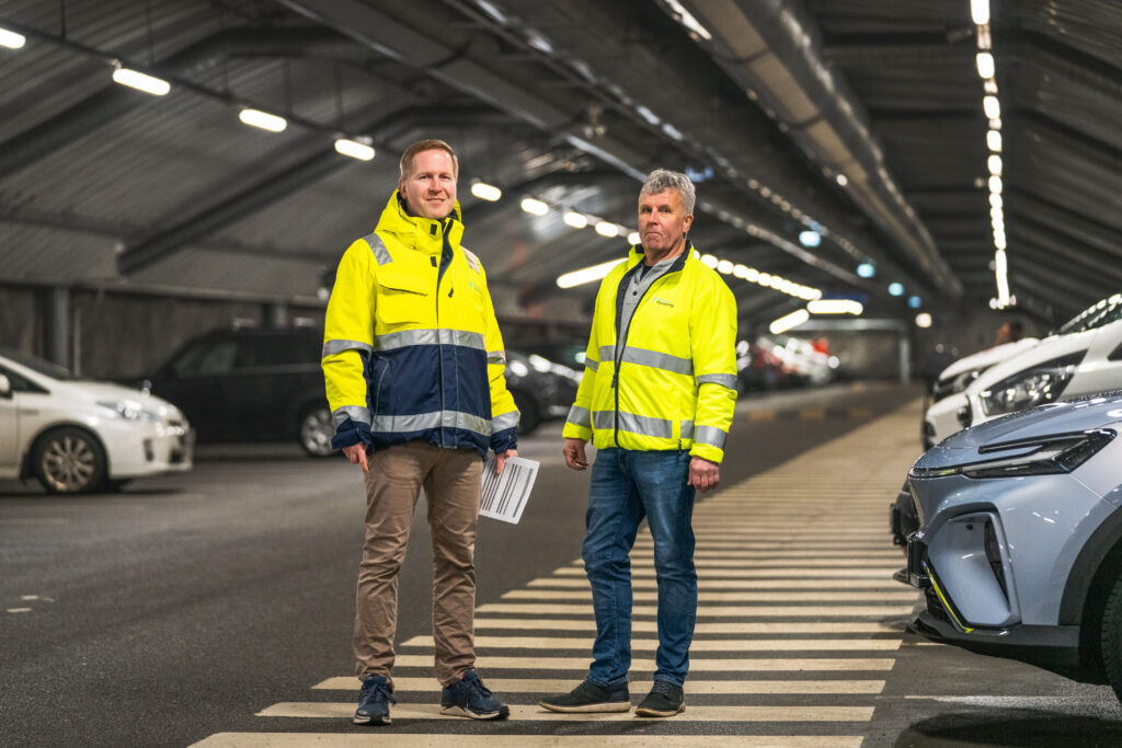 Bilde av to menn som står i KlosterGarasjen og ser mot kameraet. De har på seg synlighetstøy med logoen til Bergen Parkering på.