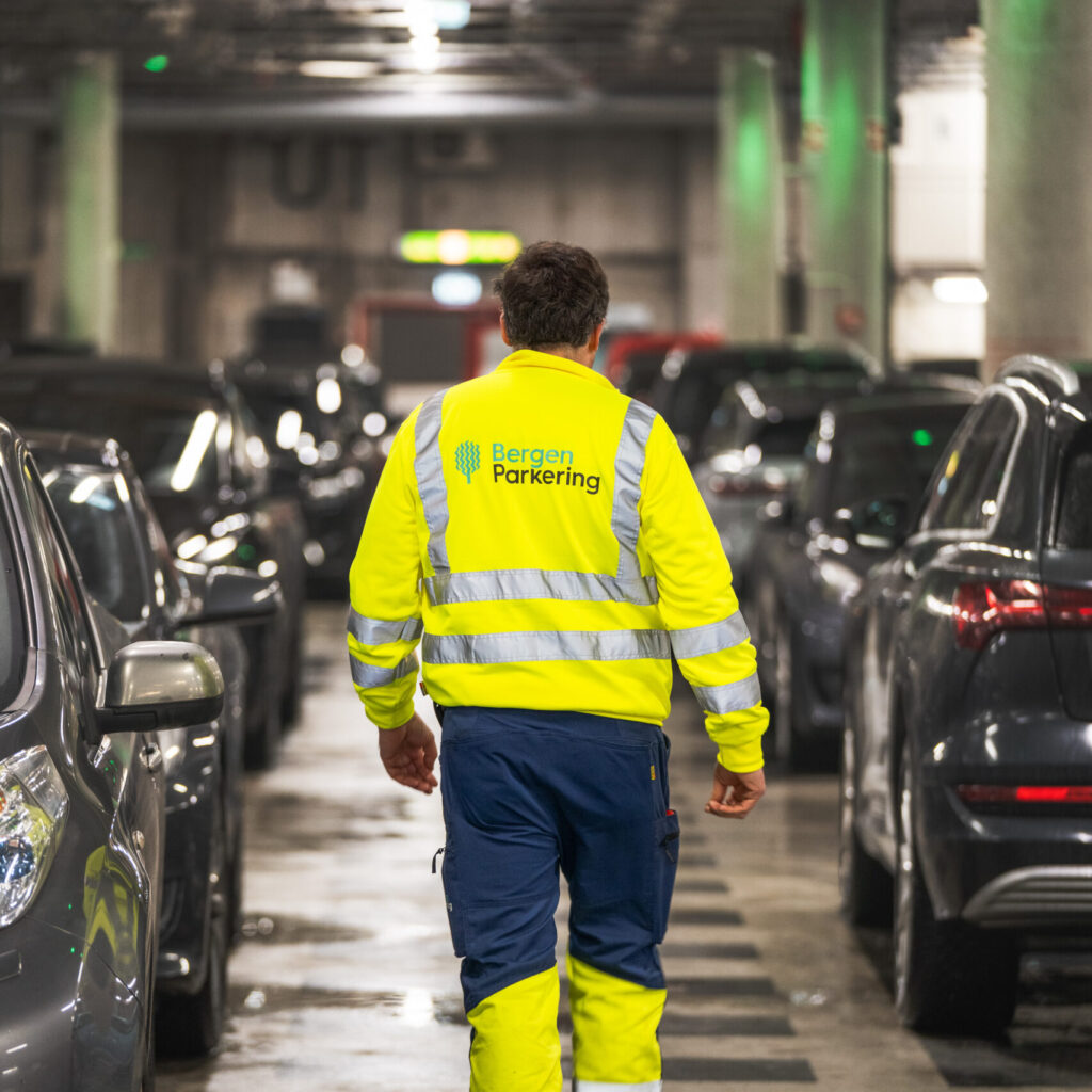 Bilde av en mann sett bakfra som går i GriegGarasjen. Han har på seg synlighetstøy med logoen til Bergen Parkering på ryggen.