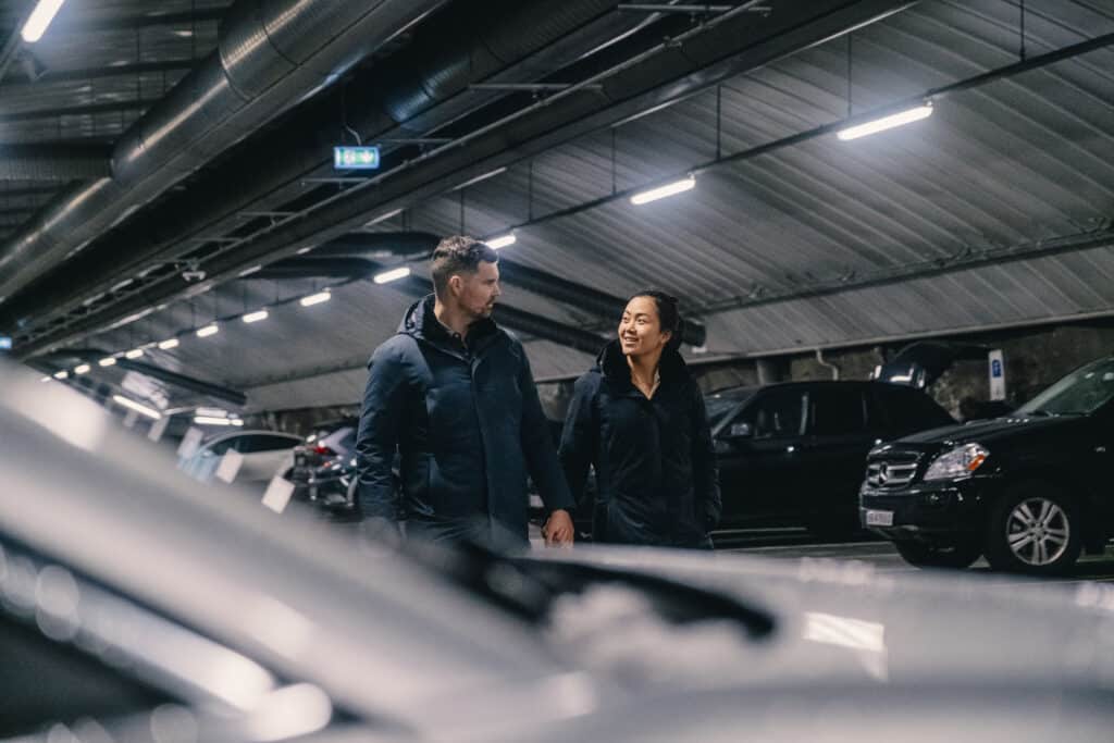 To mennesker går sammen i et parkeringshus, omgitt av parkerte biler.