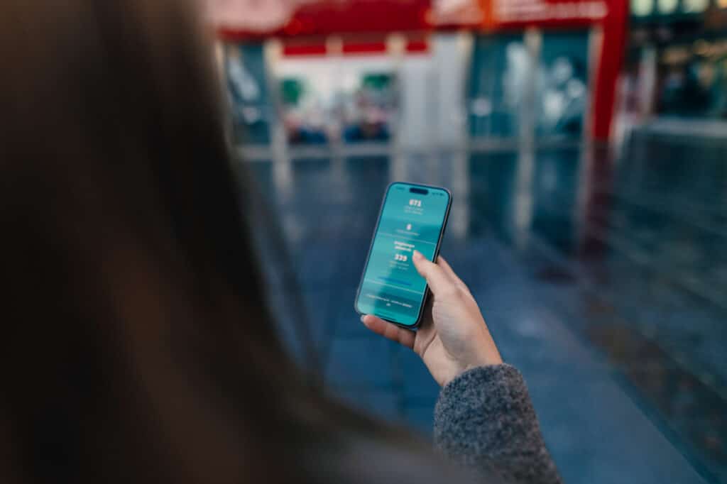 Person som holder en smarttelefon med en uskarp urban bakgrunn. På skjermen ser vi landingssiden for ledig-parkering.no.