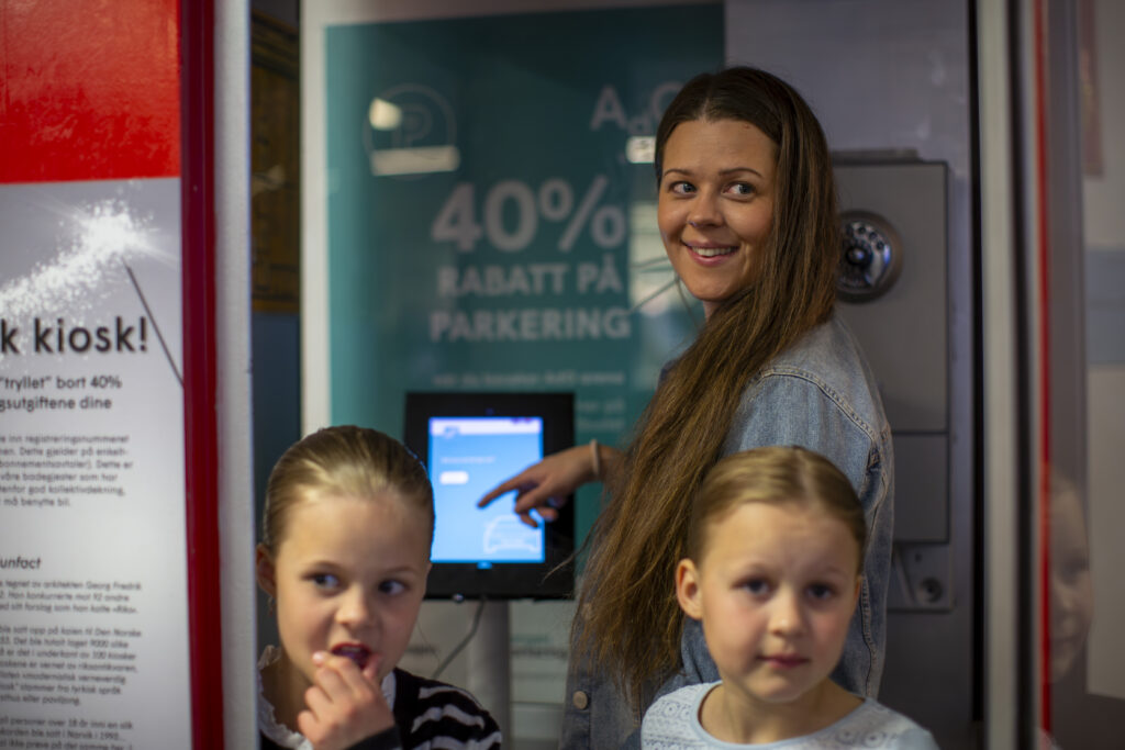 En kvinne og to små jentebarn står foran en plakat om 40% rabatt på parkering