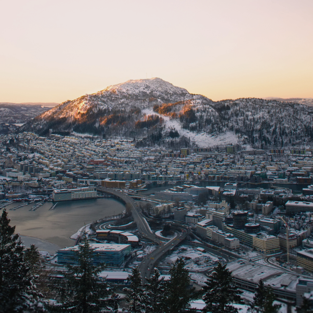 Bilde av et snødekket Bergen tatt rundt solnedgang. Man ser Løvstakken, Store Lungegårdsvann og områdene rundt.