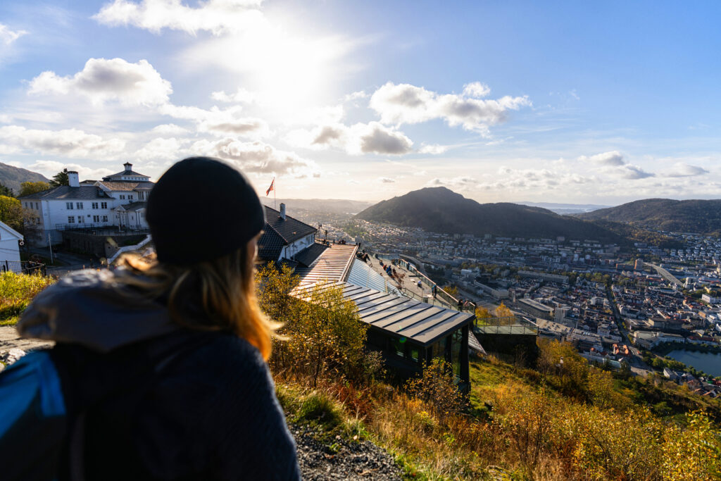 En dame står på toppen av Fløyen og ser utover mot Ulriken på en solfylt dag