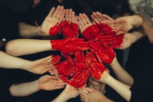 Bilde av flere menneskehender som er utstrakt mot hverandre. I midten er hendene malt i rødt for å forme et hjerte.